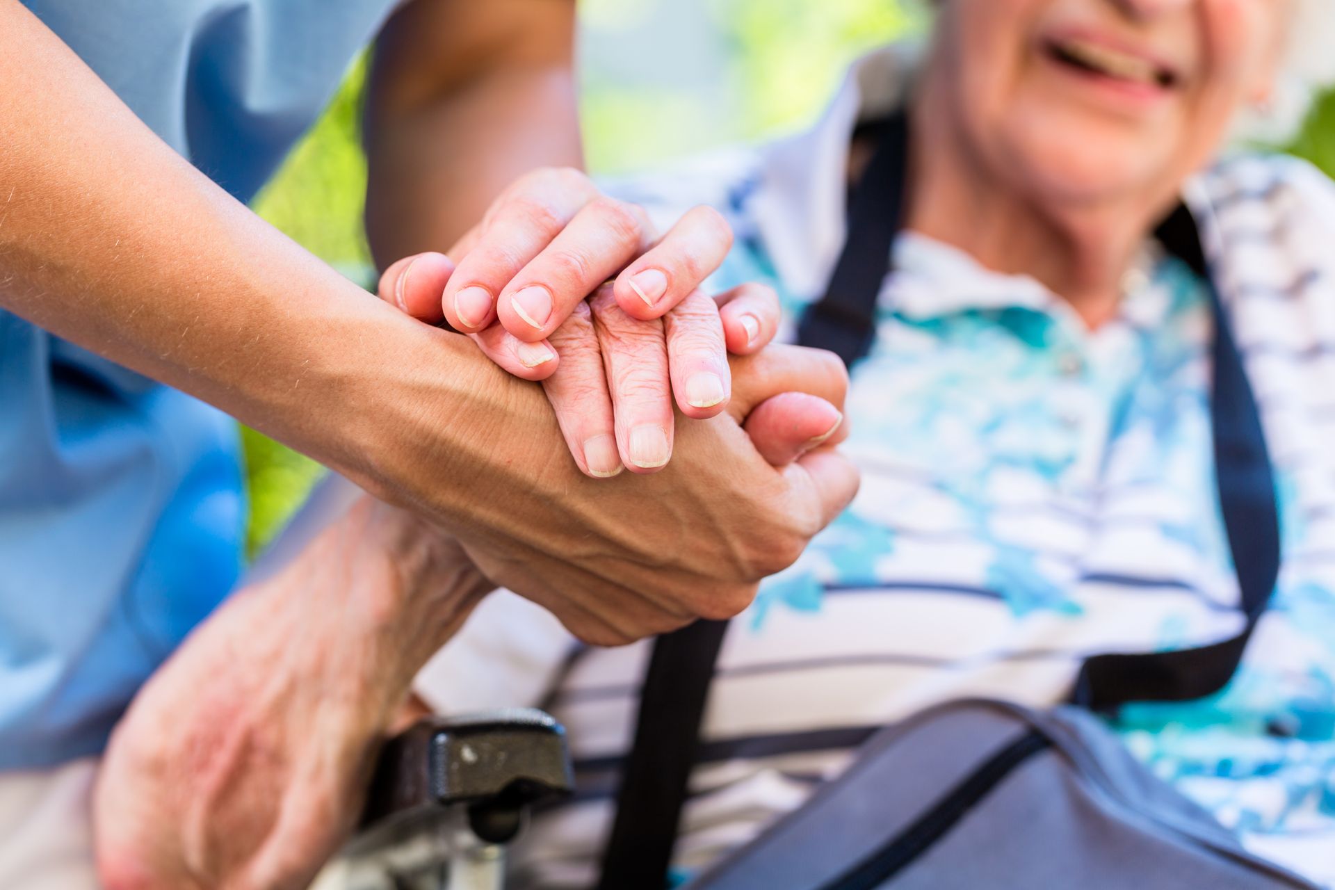 Caregiver holding hands with a person in a wheelchair outdoors.