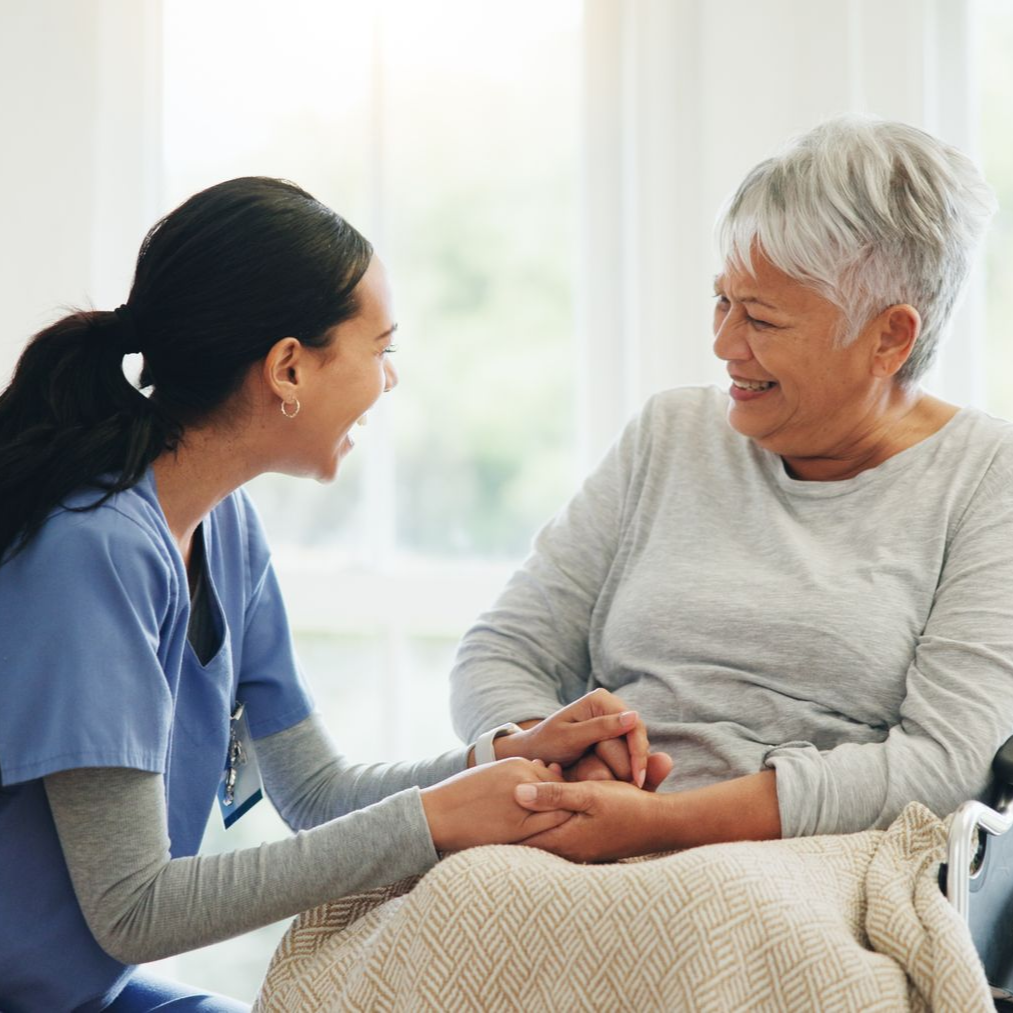 A caregiver, wearing a blue uniform, provides senior care to a senior in a wheelchair.