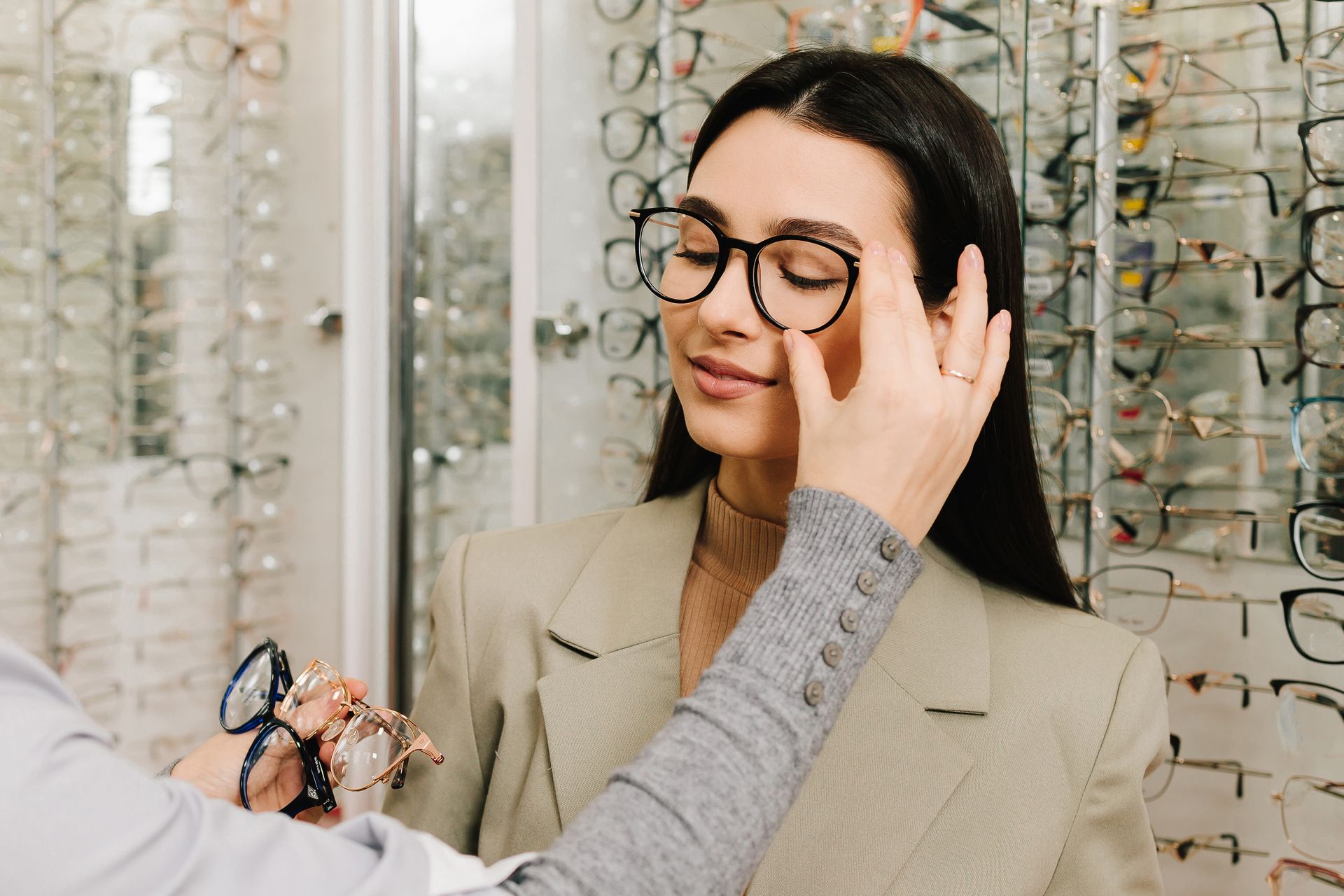 Optician adjusting glasses on a woman in a beige blazer at an eyewear shop