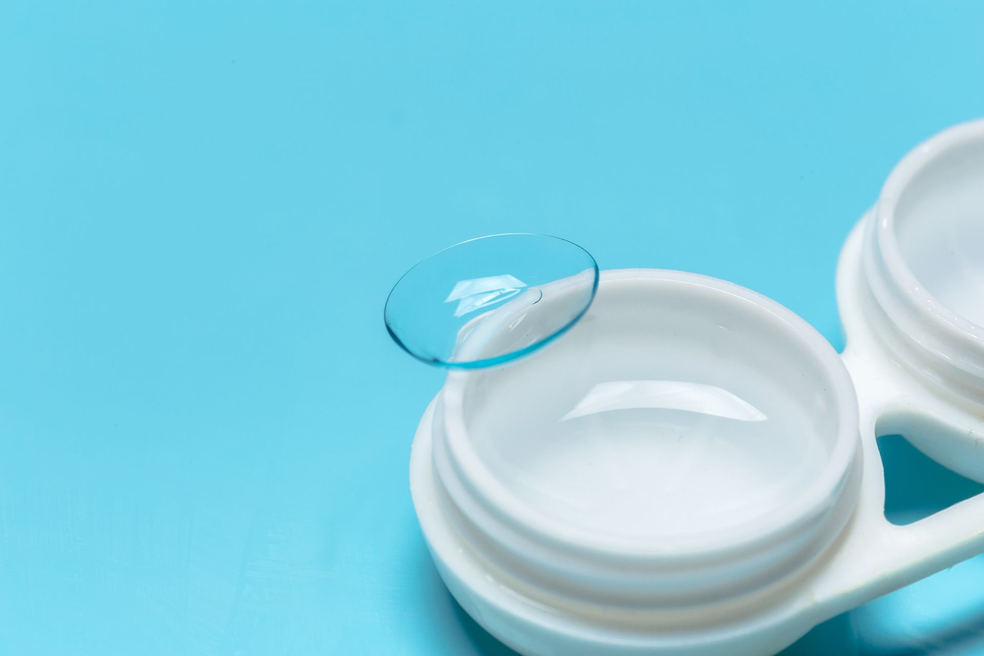 Contact lens case with a lens on the lid against a blue background
