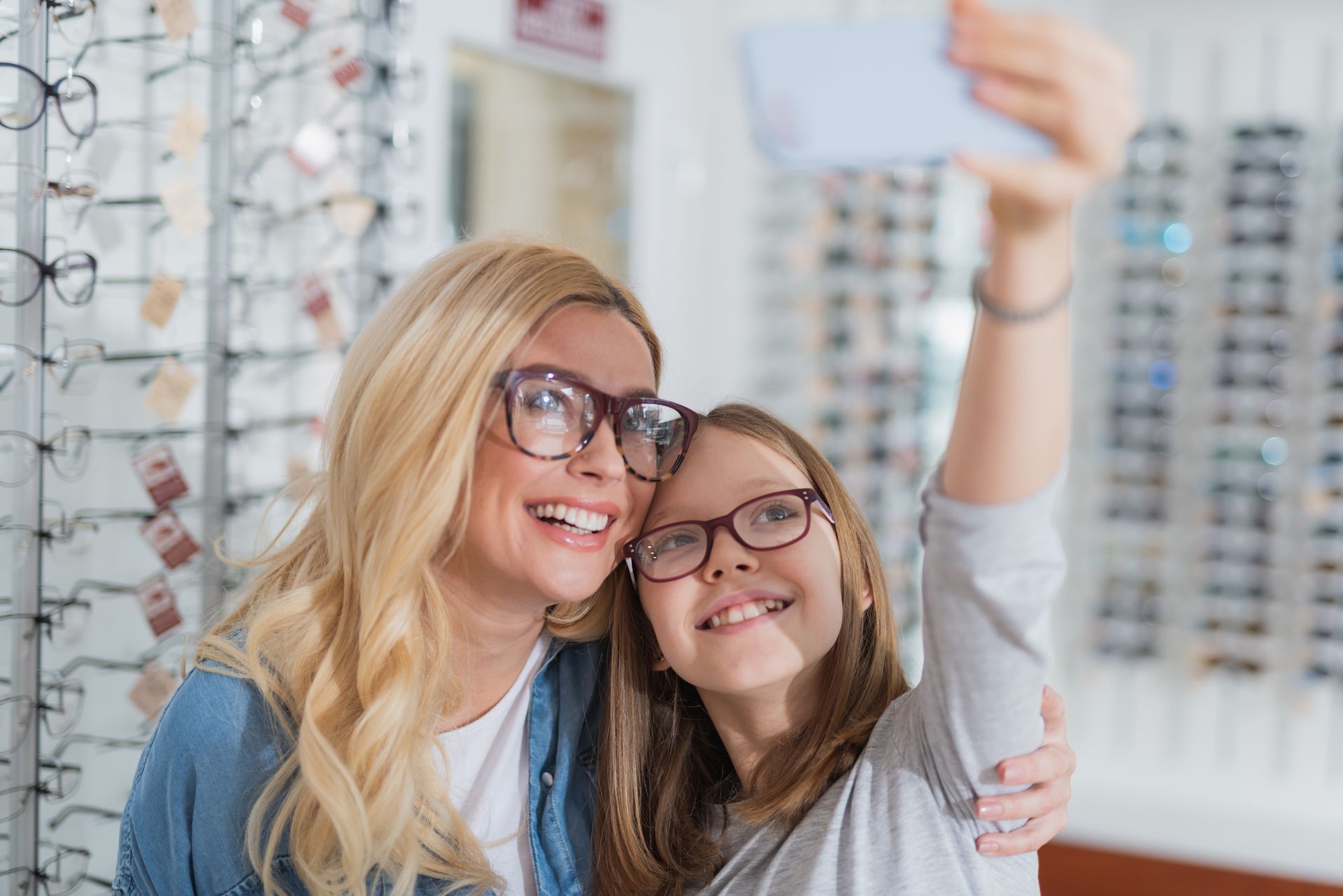 Two smiling people wearing glasses taking a selfie in an eyewear store