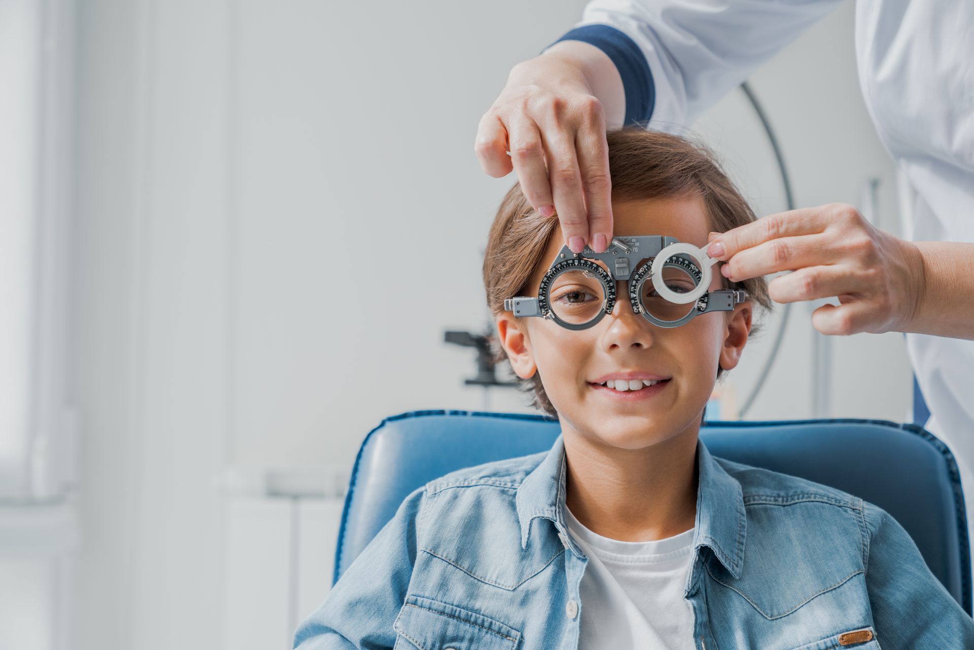Child in an optometry chair while a doctor adjusts trial lenses during an eye exam