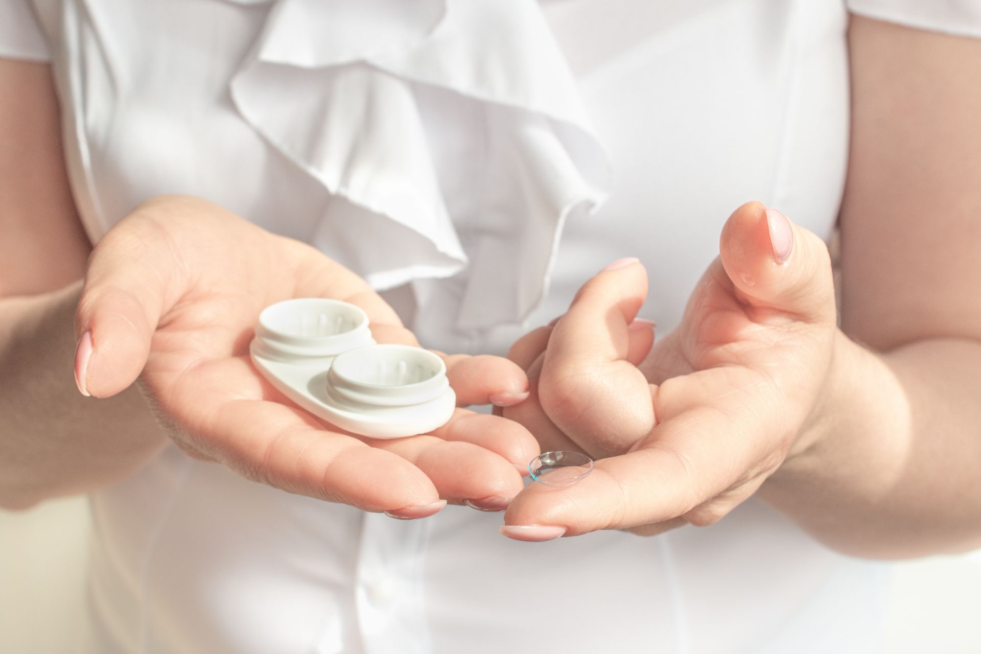 Hands holding a white prescription pill bottle and scattered tablets on a white background