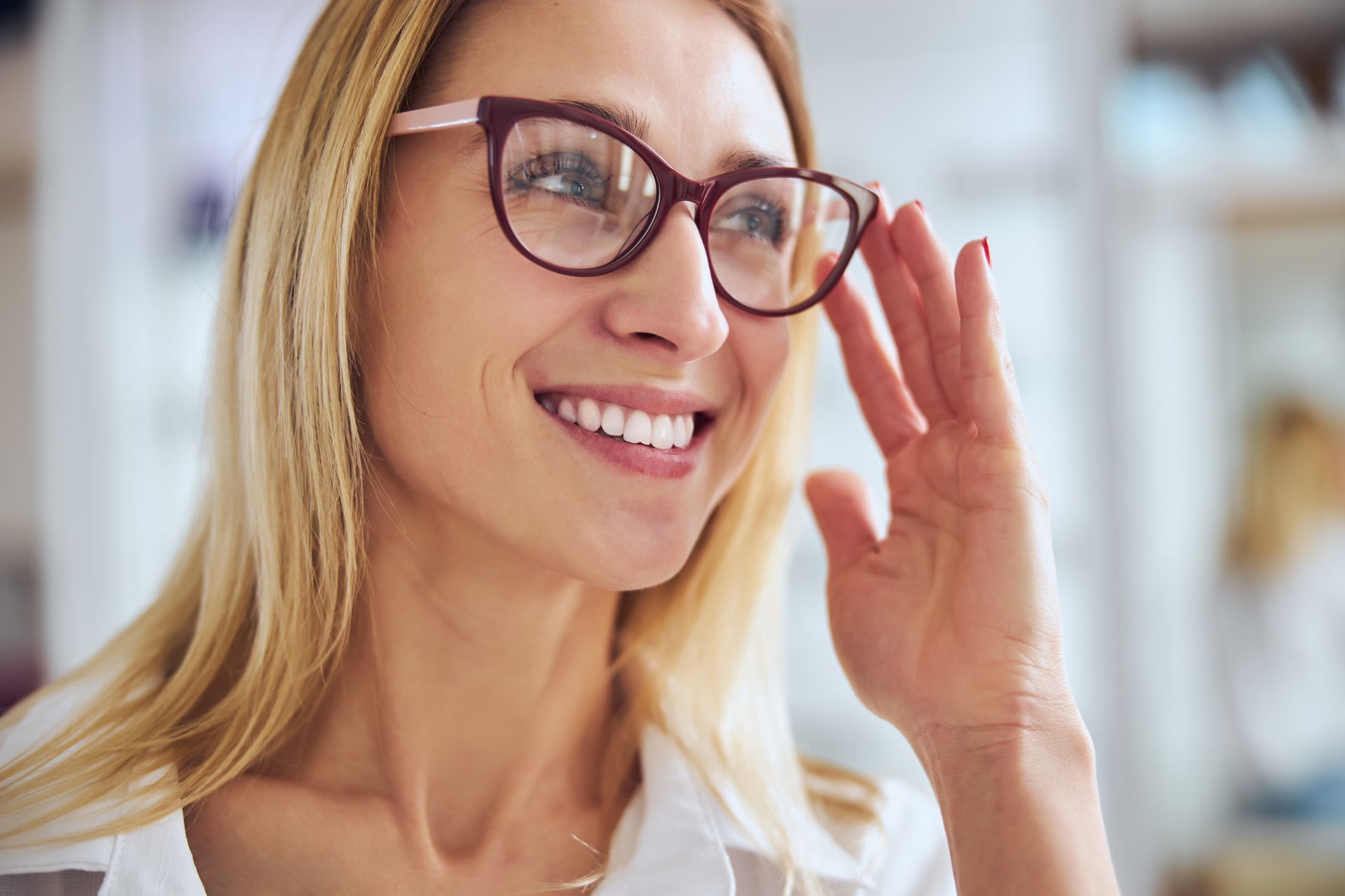 Smiling woman in glasses adjusting her frames in a bright indoor setting