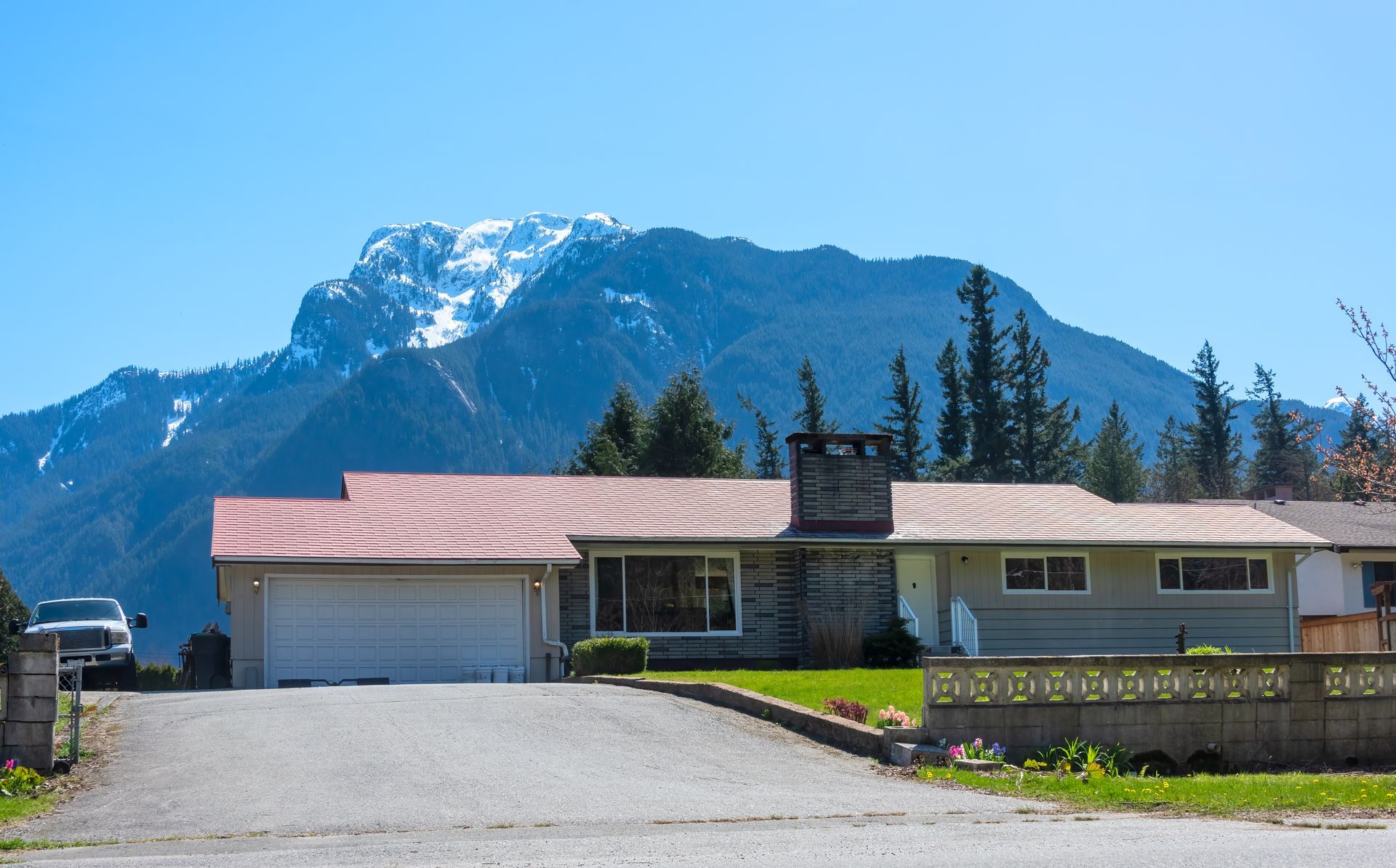 Single-story house with red roof and chimney, set before a mountain under a clear blue sky.
