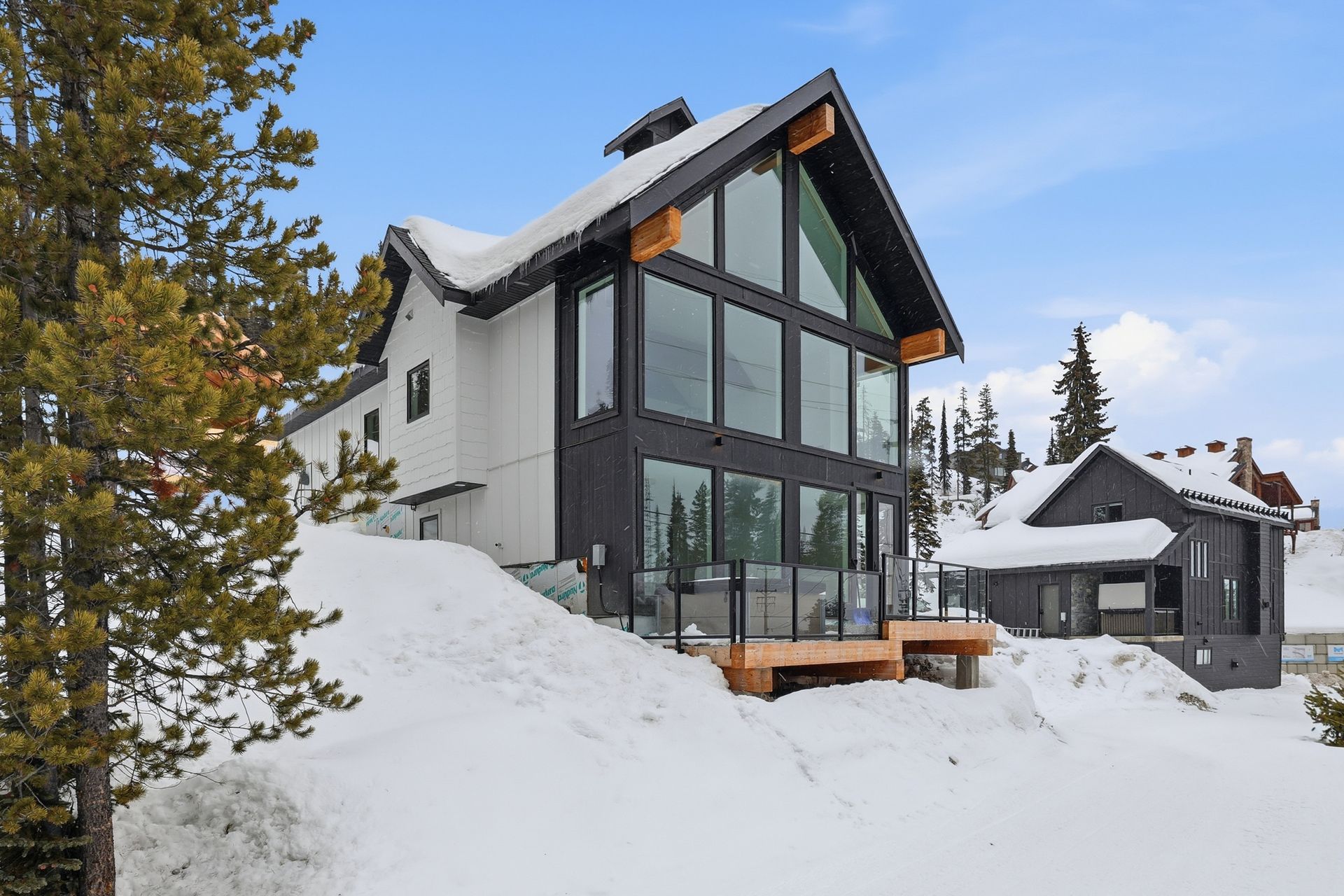Modern black-and-white mountain chalet with large windows, surrounded by deep snow and pine trees