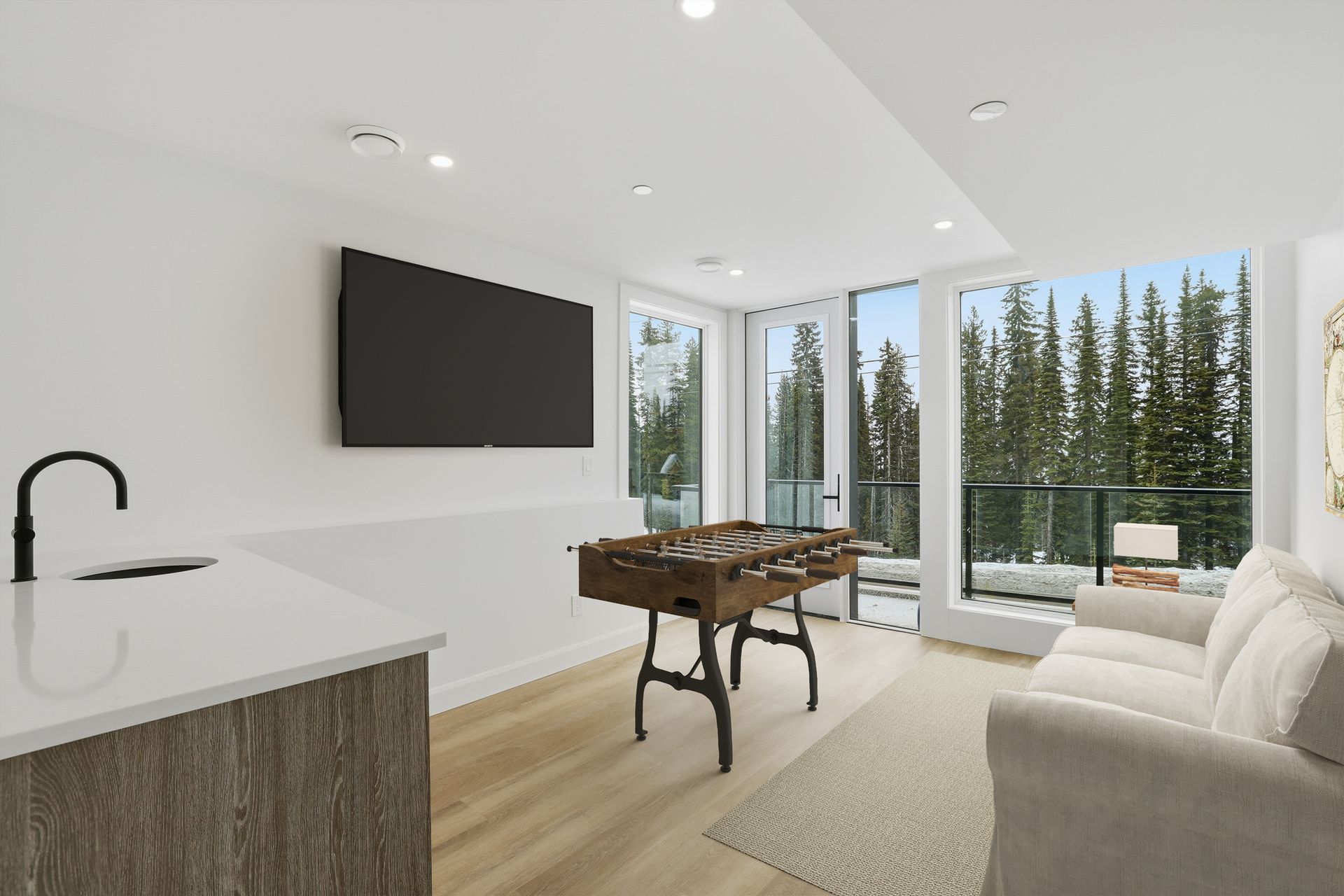 Modern bright living room with wall TV, pool table, sofa, and large windows overlooking trees