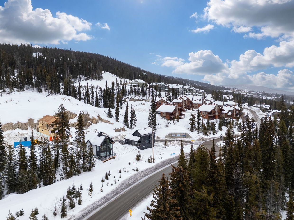 Snowy mountain resort with cabins, pine trees, and a road under a blue sky