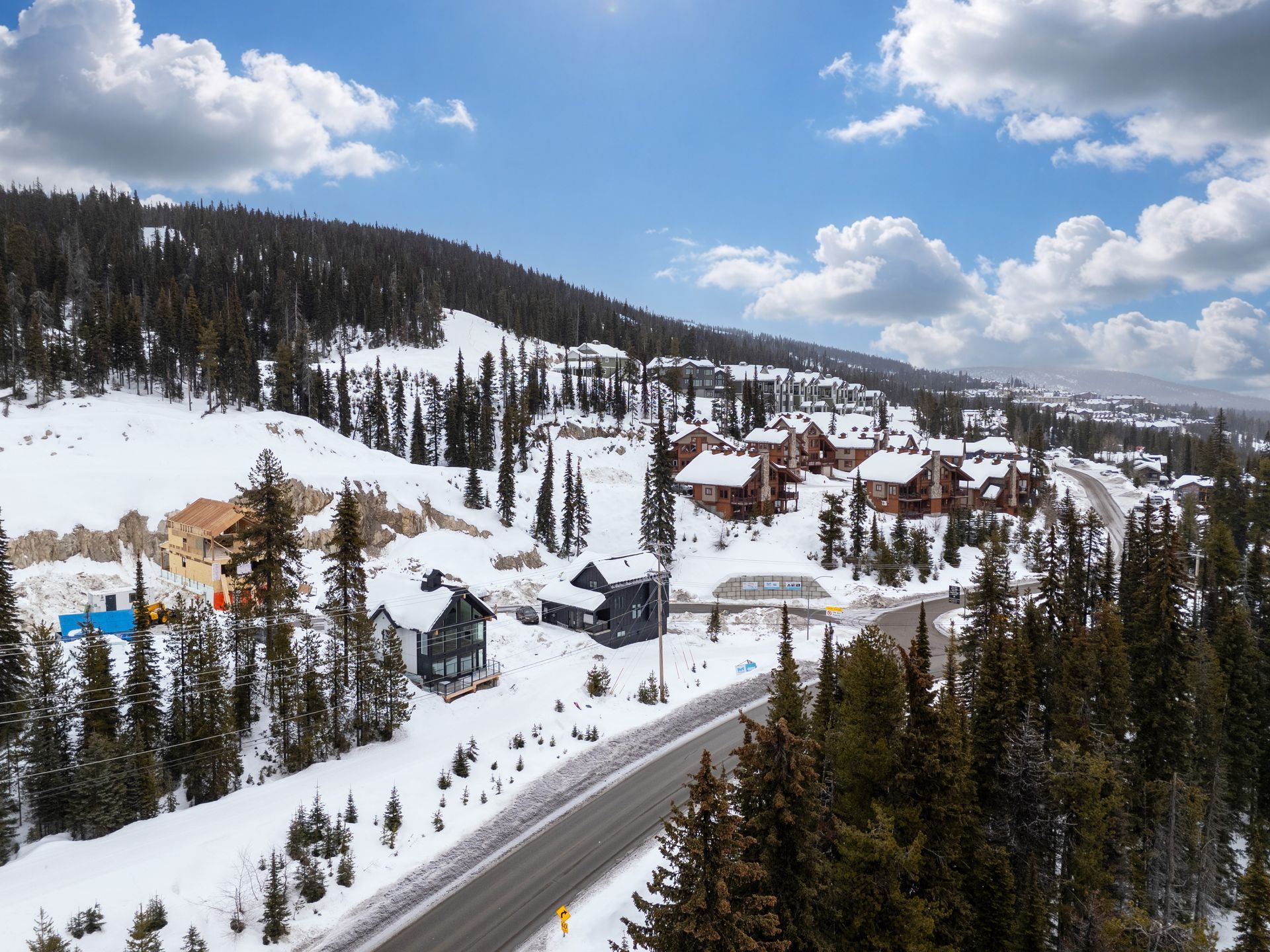 Snowy mountain resort with cabins, pine trees, and a road under a blue sky