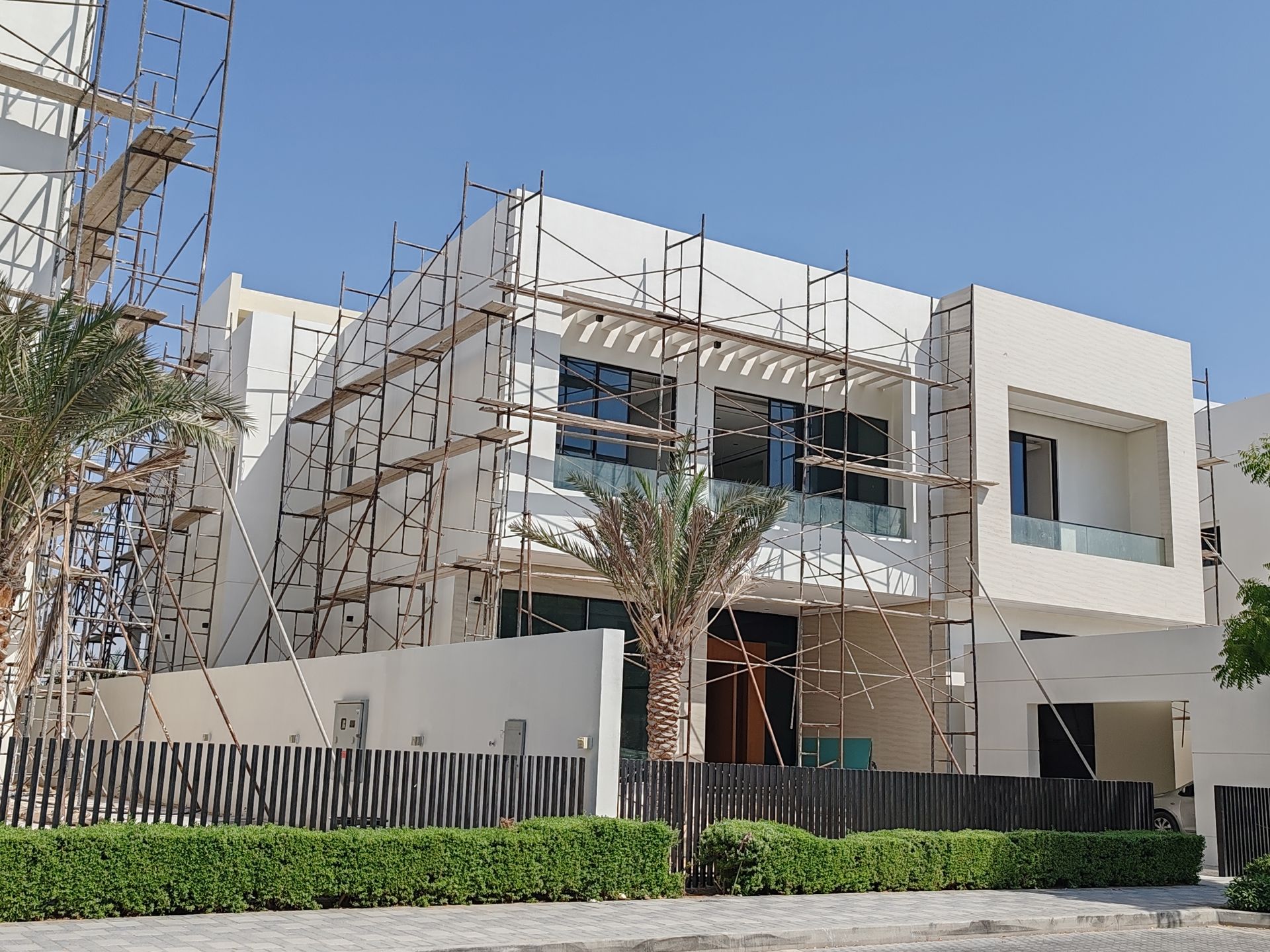 Modern white two-story house under construction with scaffolding and a palm tree in front