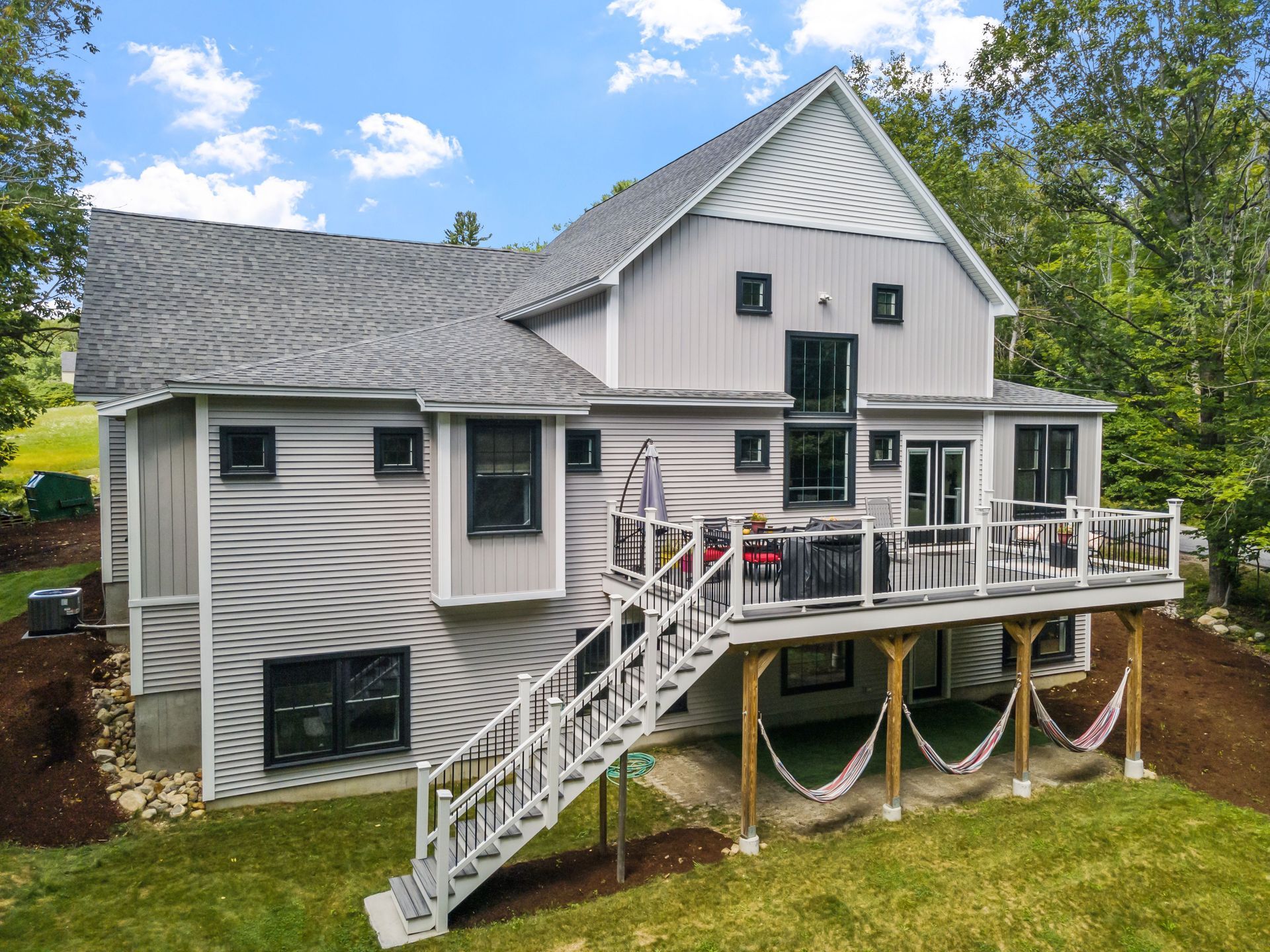 White two-story house with gray roof and deck, viewed from the yard under a blue sky.