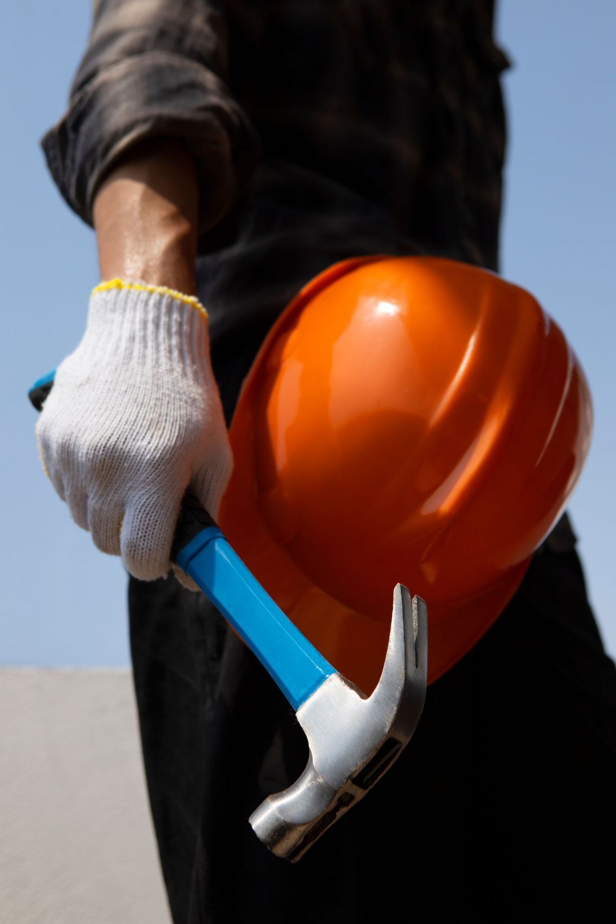 Gloved worker holding a hammer and orange hard hat against a plain background