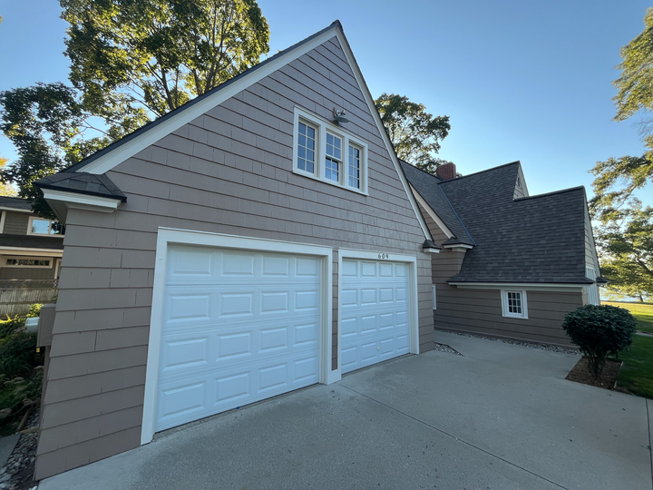Two-car garage with white doors on a gray shingle house, viewed from the driveway