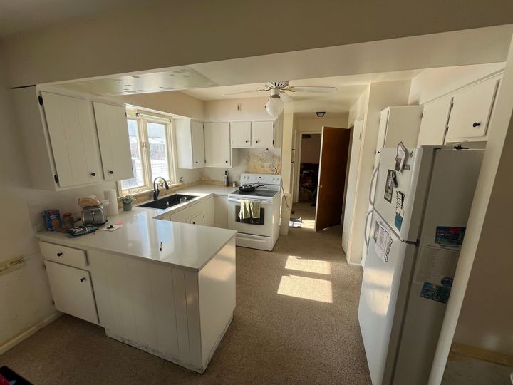 Bright kitchen with white cabinets, island, stove, and refrigerator in a sunlit home interior