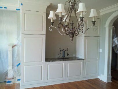 Built-in white cabinets with granite countertop, chandelier above. Room has wooden floor and archway.