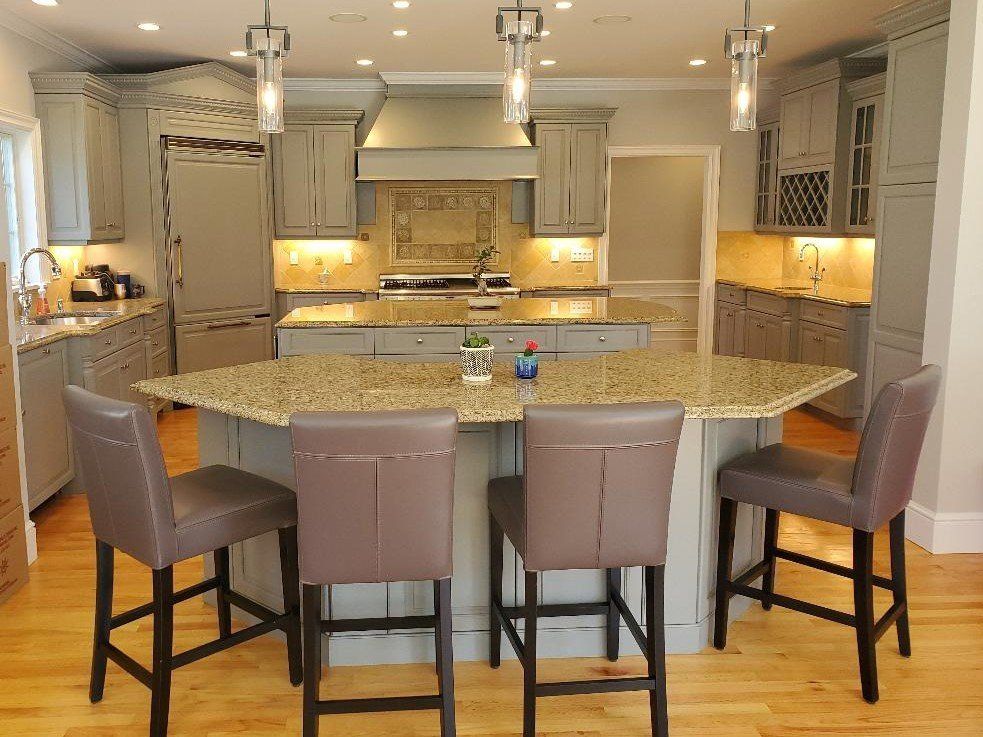 A well-lit kitchen with gray cabinets, a granite countertop island with four bar stools, and pendant lights.