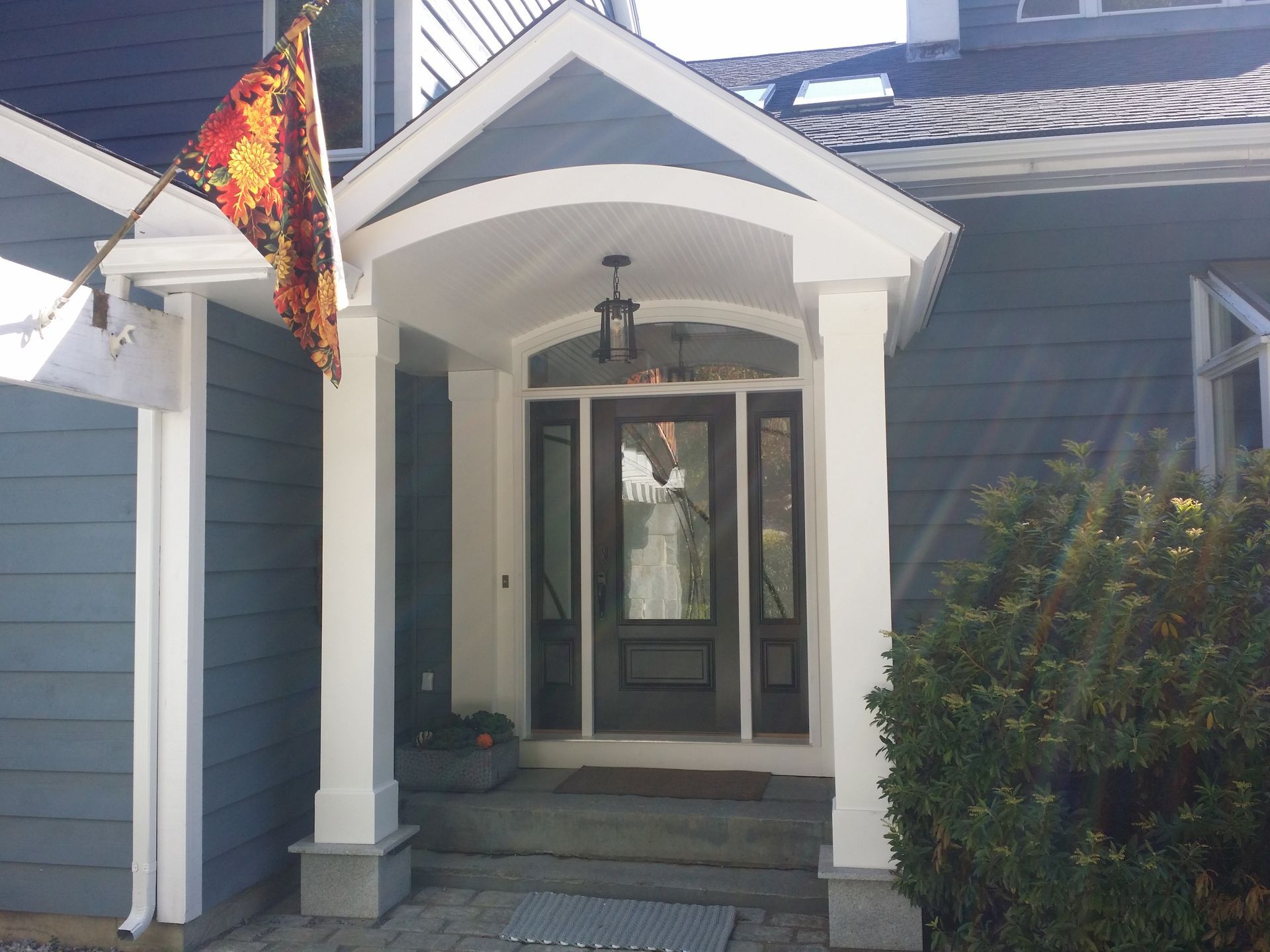 Blue house entrance with a covered doorway, glass door, and flag.