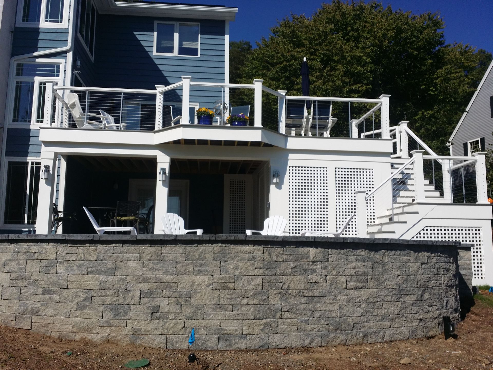 Backyard deck with white railings, a blue house, and a stone retaining wall.