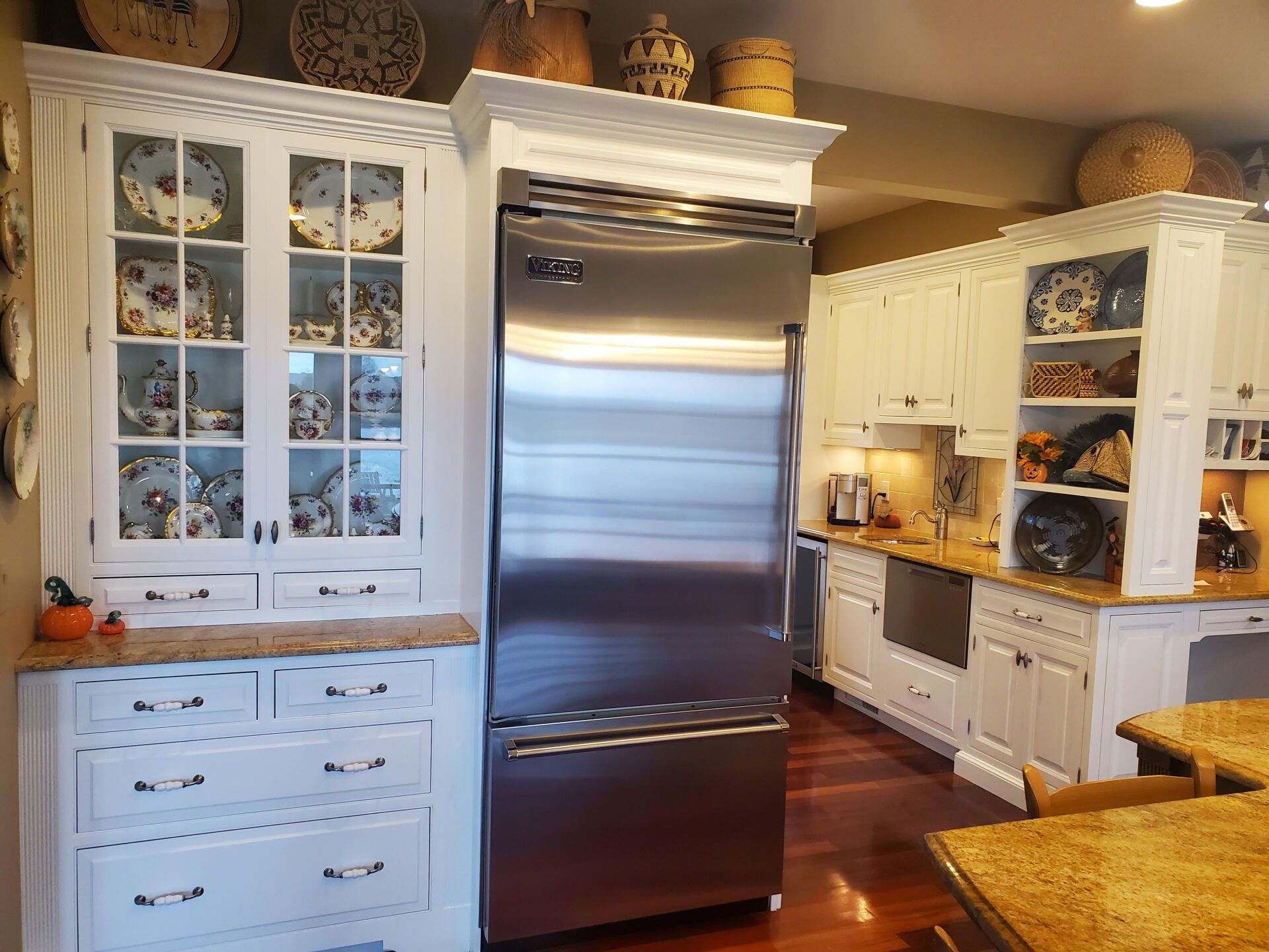 Stainless steel refrigerator in a white kitchen with cabinets and wood floors.