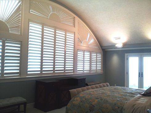 Bedroom with arched window and white shutters, dresser, and a bed with floral bedding.