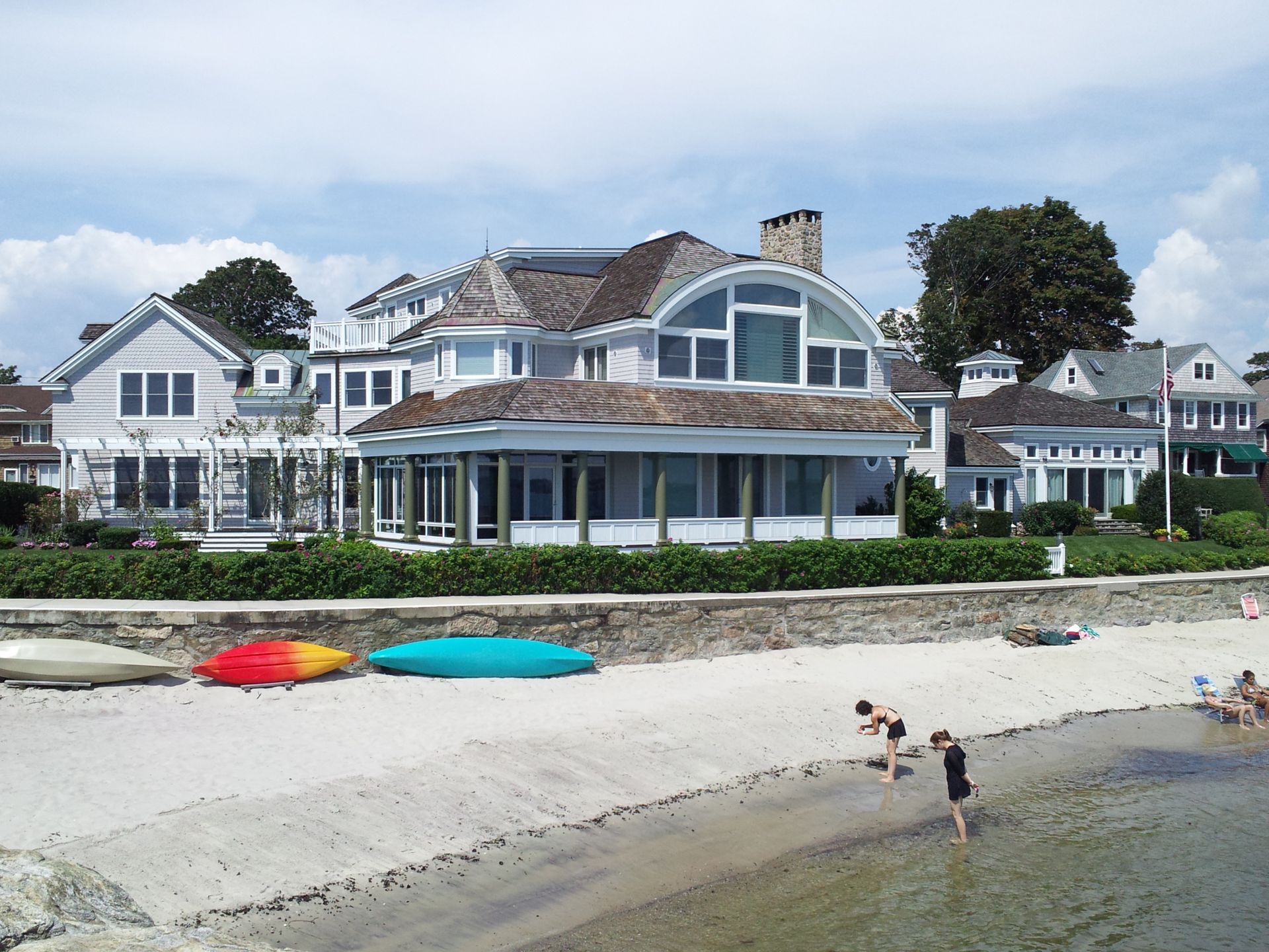 Beachfront homes with sandy shore, kayaks, and people.