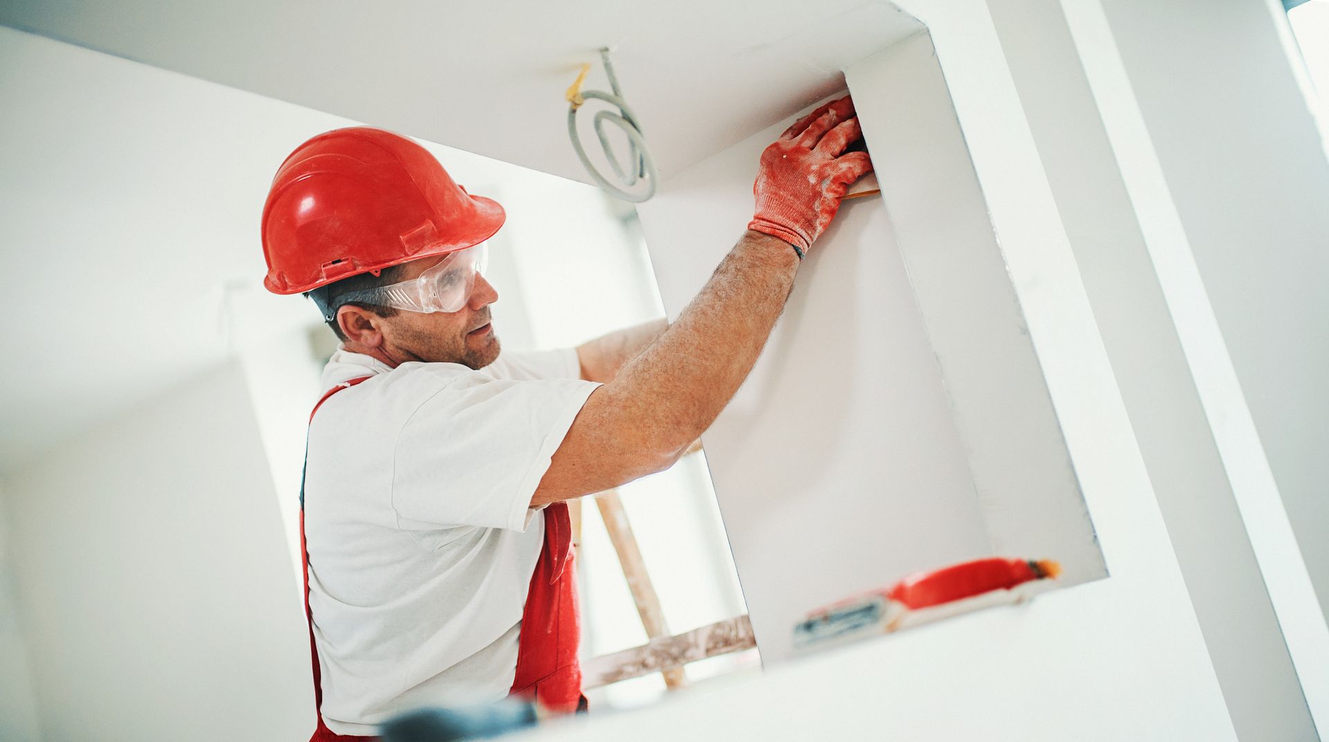 A man wearing a hard hat and safety glasses is working on a wall.