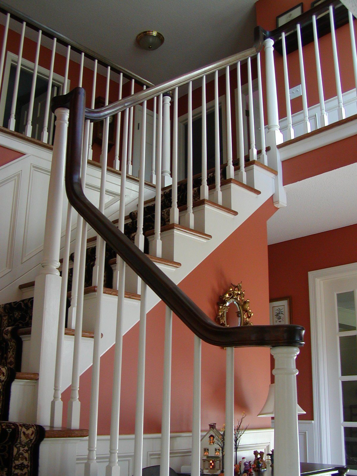 Staircase with white balusters, brown handrail, and orange walls.