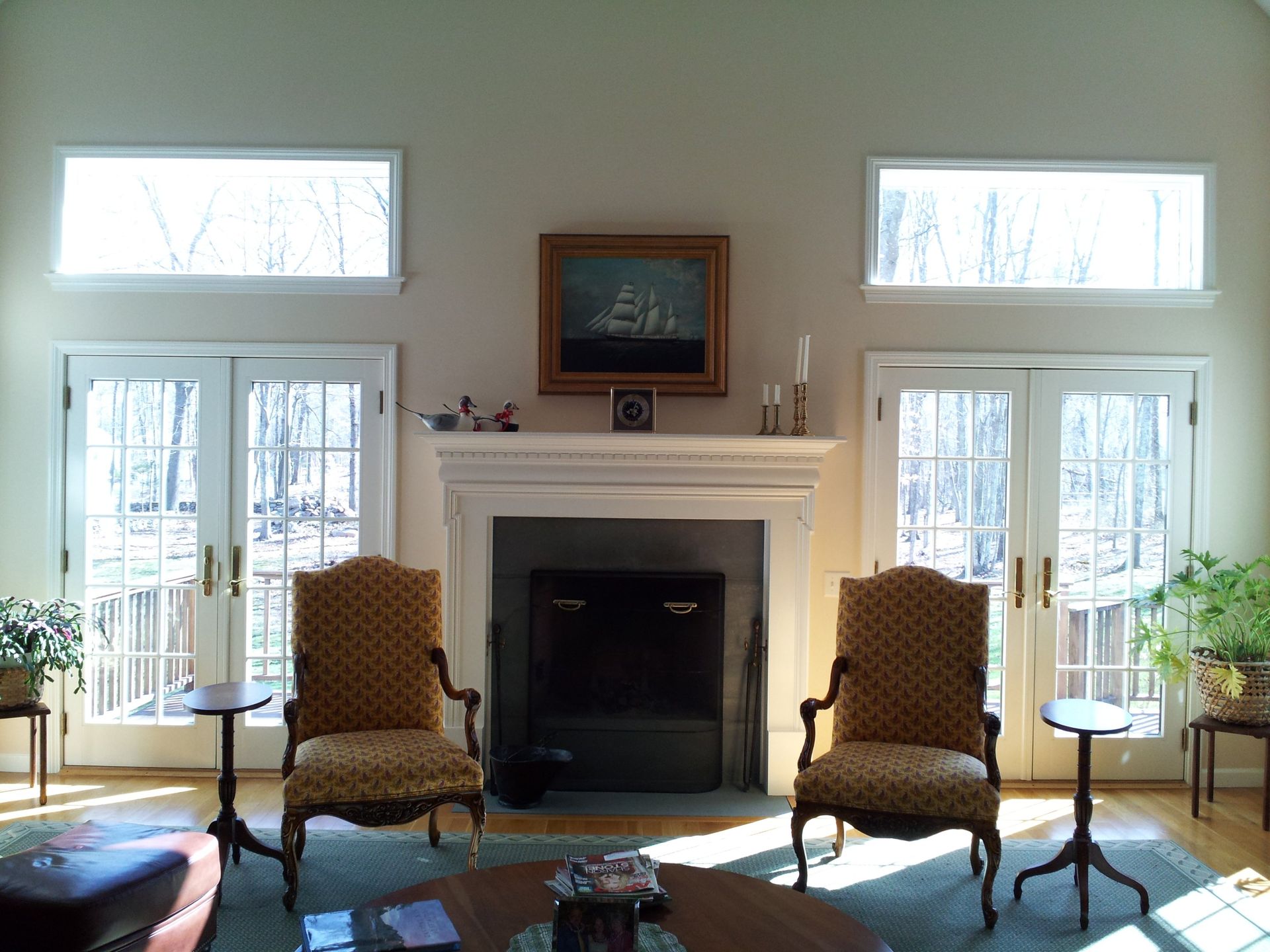 Living room with fireplace, French doors, two chairs, and two high windows.