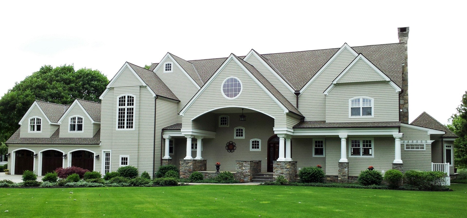 Large house with multiple gables, pillars, and a green lawn.