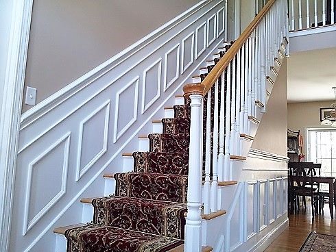 Staircase with white trim, tan wall, and patterned runner. Wooden railing and light wood floor visible.