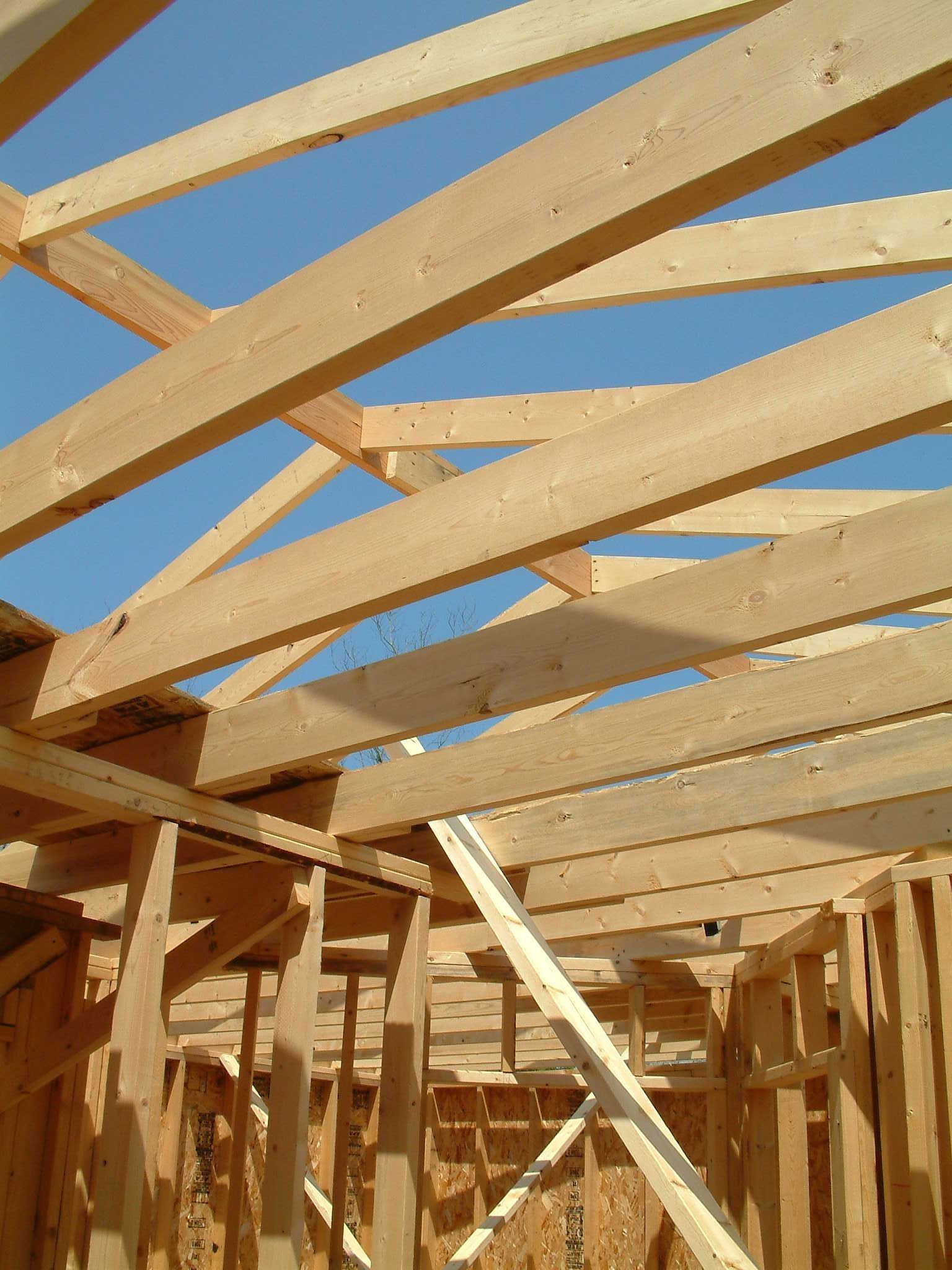 Wooden roof trusses being installed on a house under construction against a blue sky