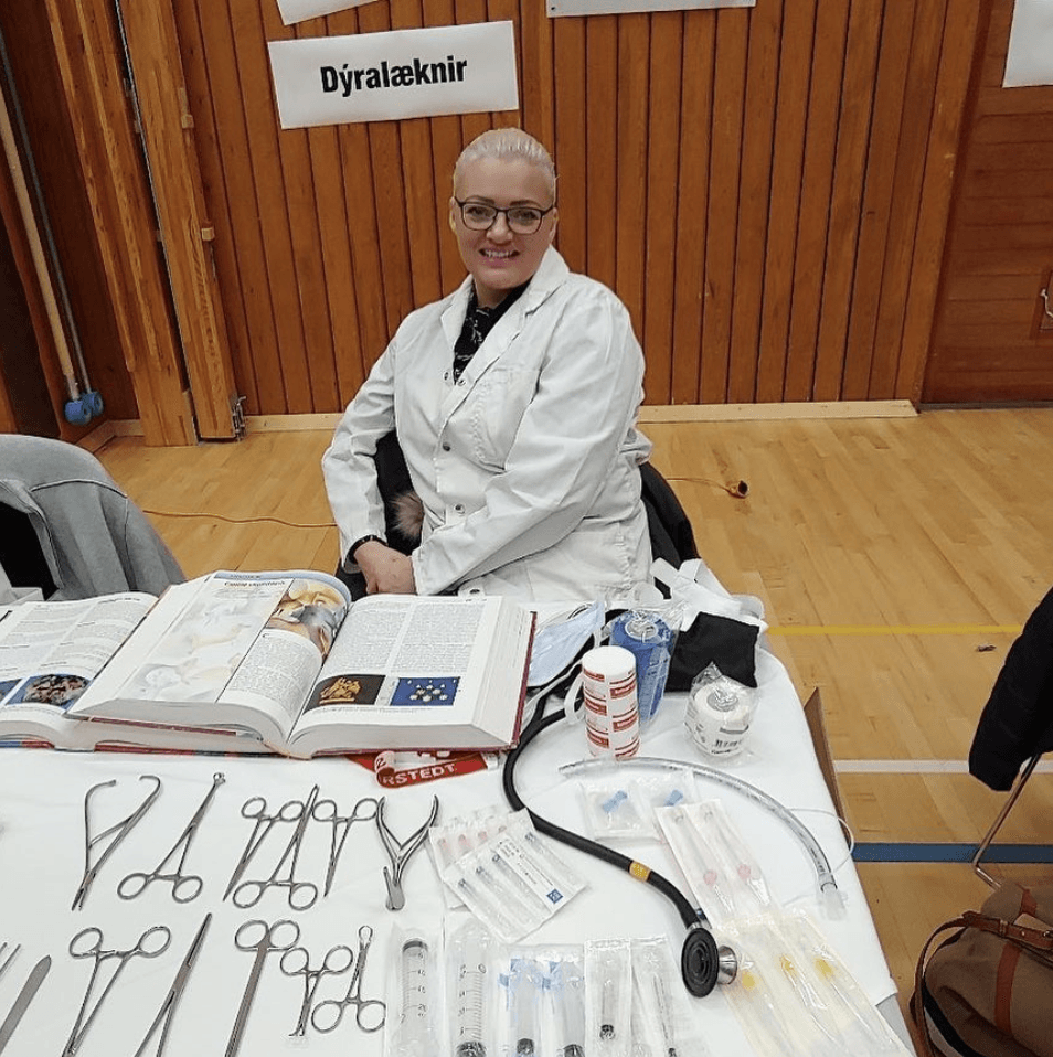 Woman in lab coat at table with medical instruments, open book.