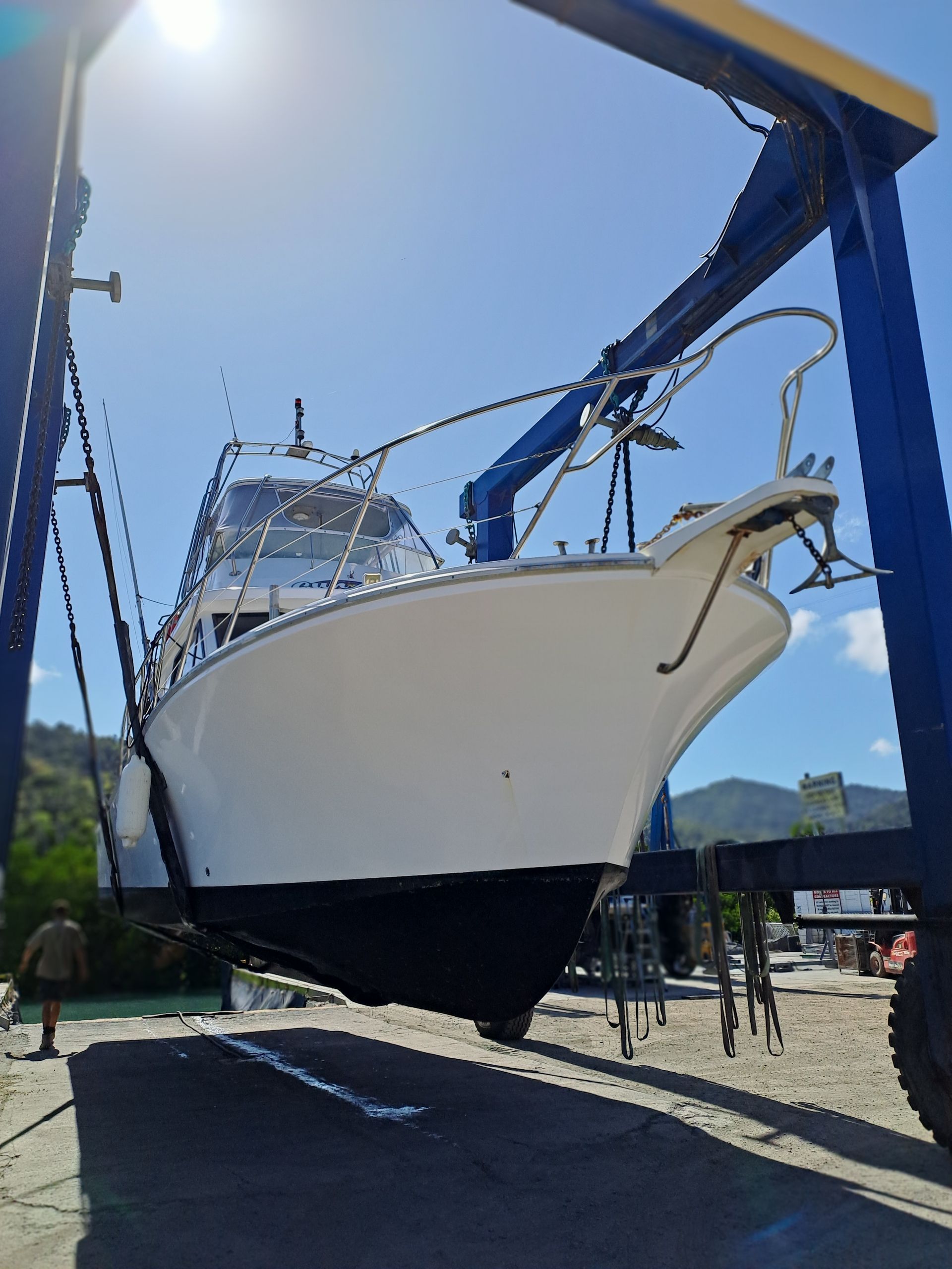 A white boat is being lifted by a blue crane — Edge's Boatyard In Jubilee Pocket, QLD
