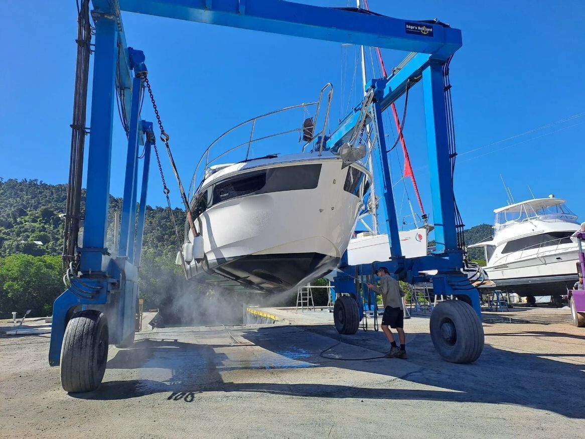 A Boat Is Being Lifted By A Crane And A Man Washing the Bottom Of The Boat — Edge's Boatyard In Airlie Beach, QLD