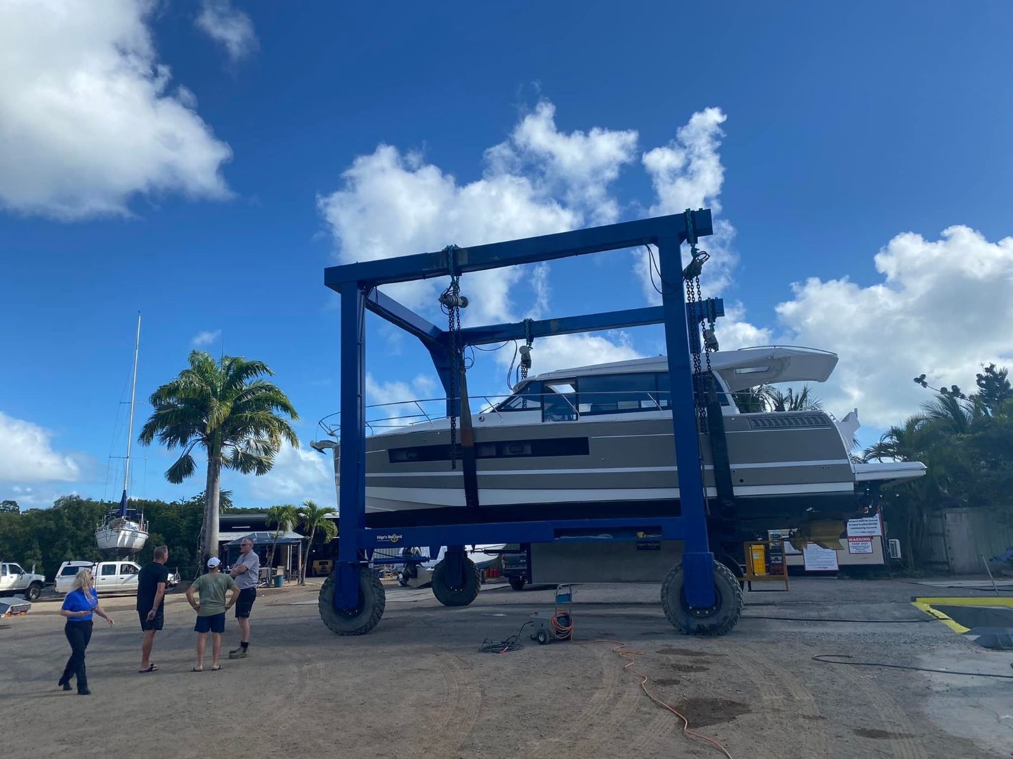 A Boat Is Being Lifted By A Crane And 3 Men Talking In A Parking Lot — Edge's Boatyard In Whitsundays, QLD