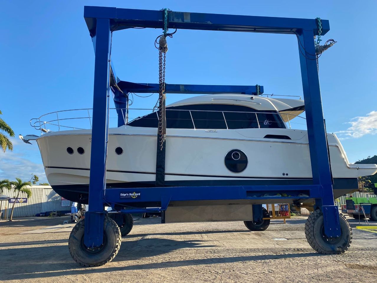 A White Boat Is Being Lifted By A Blue Crane — Edge's Boatyard In Whitsundays, QLD
