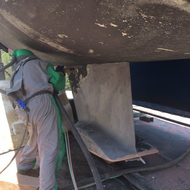 A Man Wearing A Green Apron Is Sandblasting A Boat — Edge's Boatyard In Whitsundays, QLD