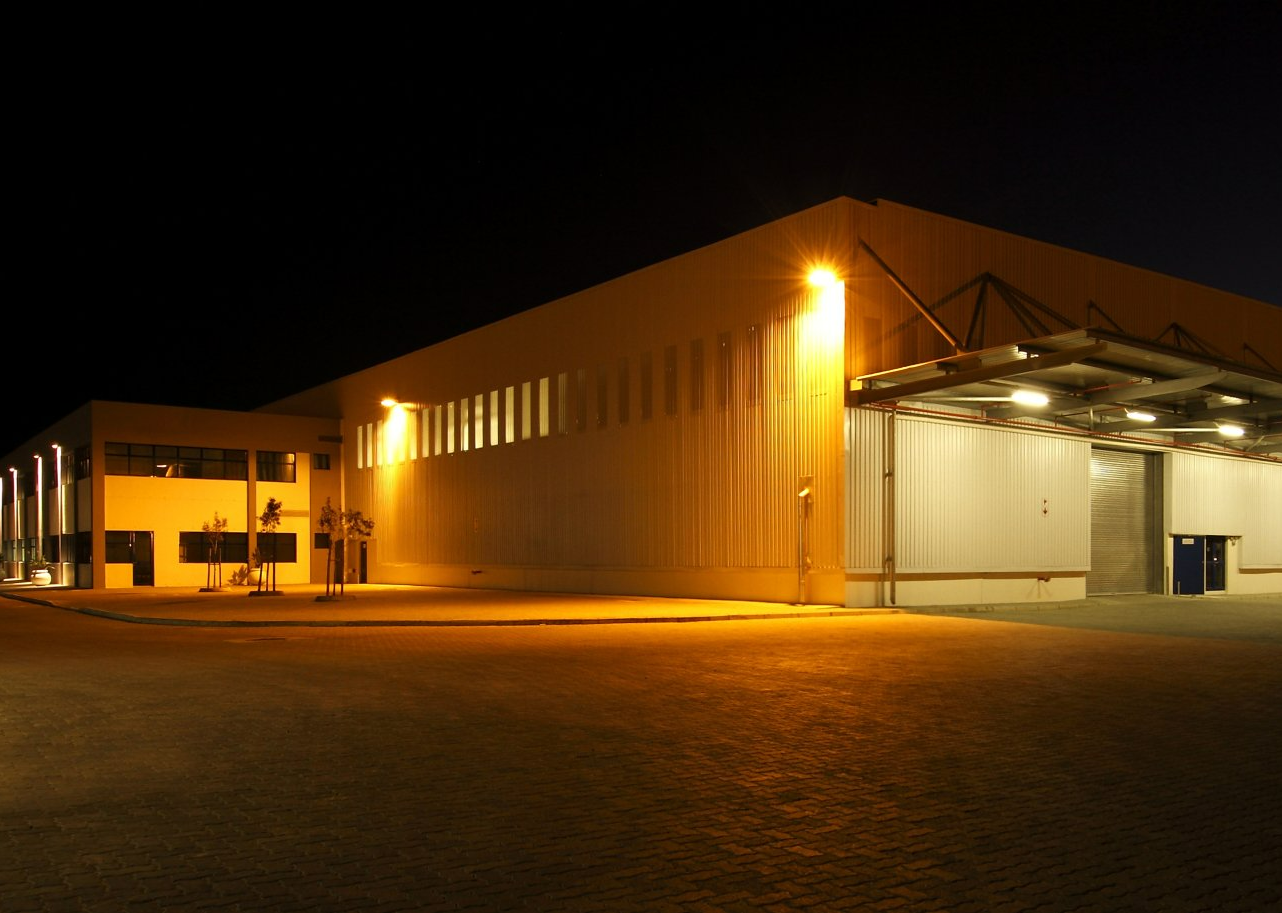 Nighttime view of a large industrial warehouse lit by bright orange exterior lights