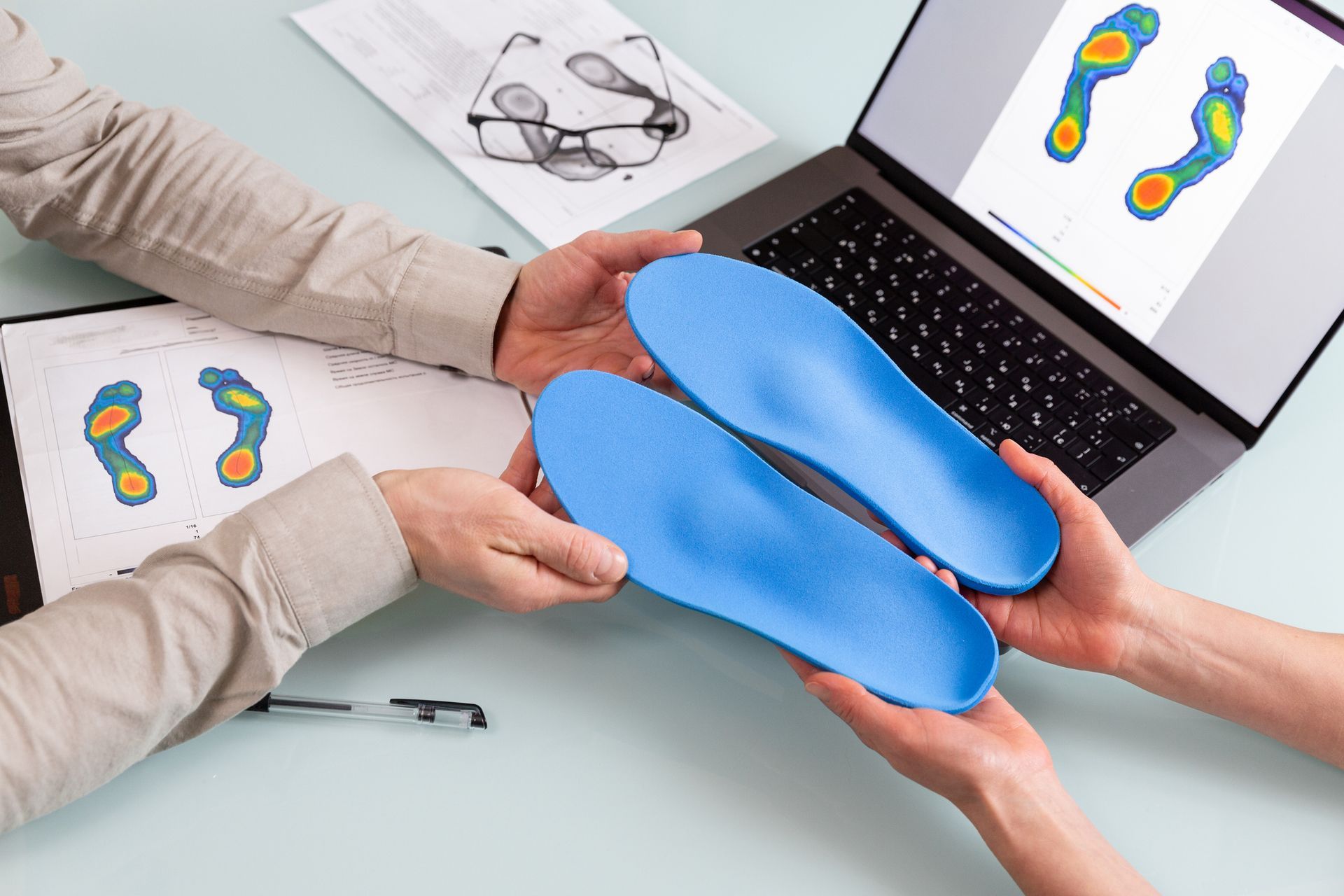 Due persone esaminano i plantari blu delle scarpe insieme alle analisi della scansione del piede su un computer portatile e su un foglio di carta.