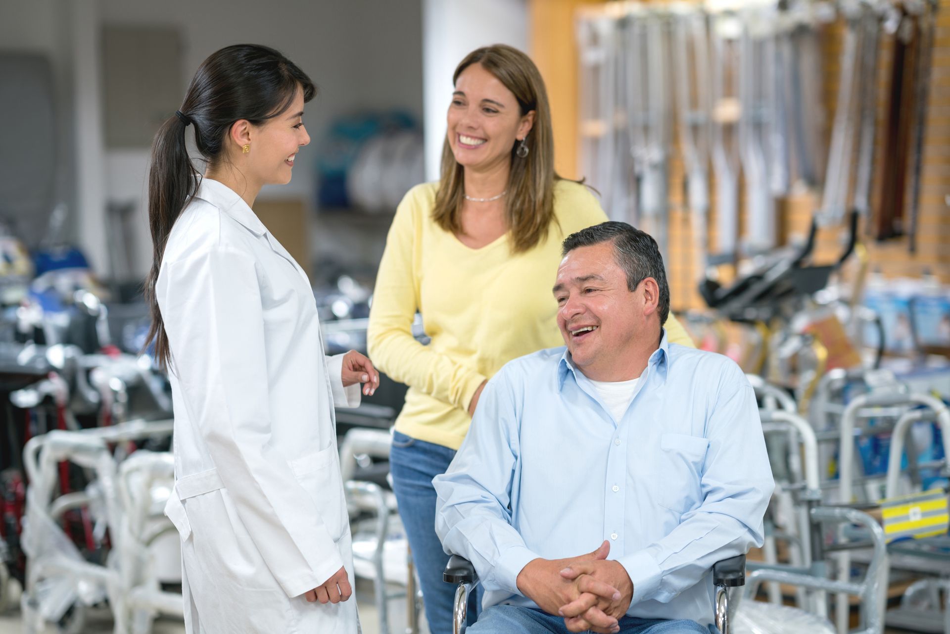 Una donna in camice da laboratorio aiuta un uomo sulla sedia a rotelle e una donna in un negozio di forniture mediche.