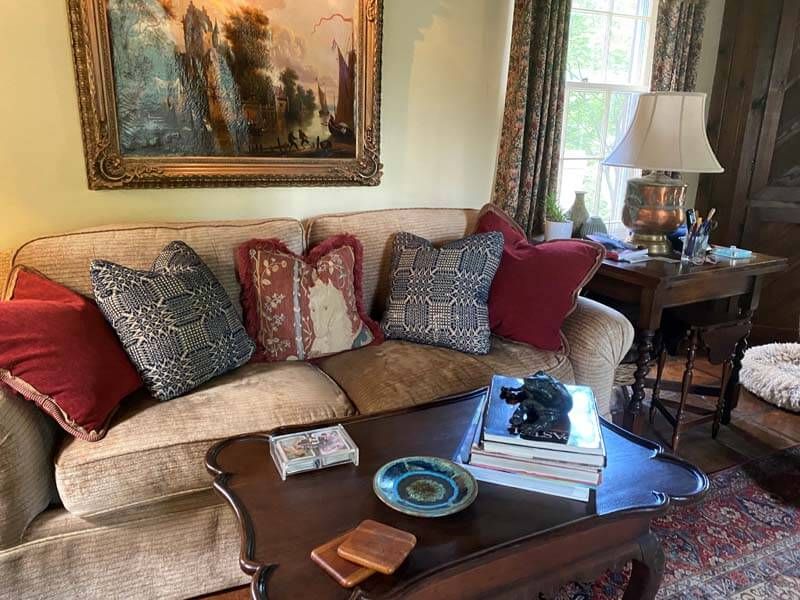 Cozy living room with beige sofa, patterned pillows, coffee table, lamp, and framed painting above.
