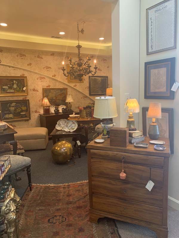Cozy antique-filled living room with chandelier, lamps, patterned rug, and wooden side table