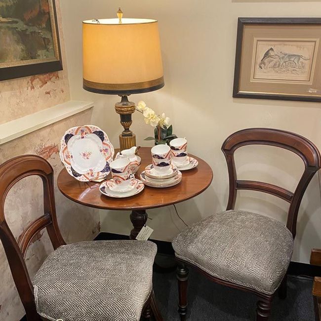 Small round tea table set with china, lamp, and two upholstered chairs in a cozy corner.