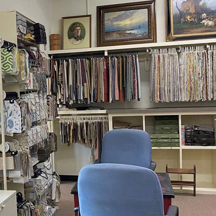 Fabric shop interior with shelves of textiles, hanging cloth samples, and two blue chairs in front.