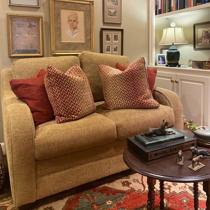 Cozy living room with tan sofa, patterned pillows, side table, lamp, and framed wall art.