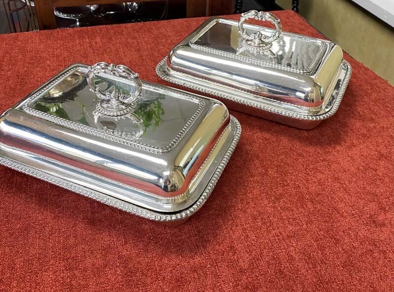Two silver serving trays with lids on a red tablecloth