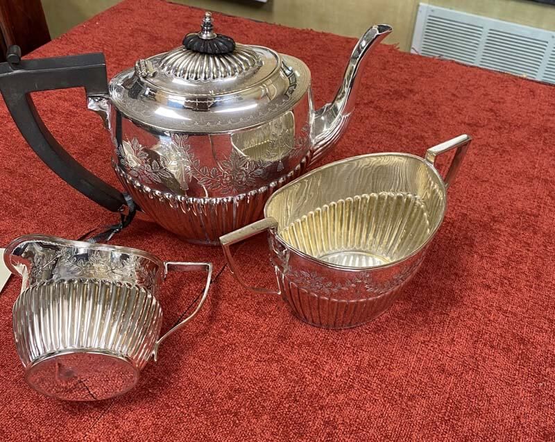 Silver tea set with teapot and two creamers on a red tablecloth