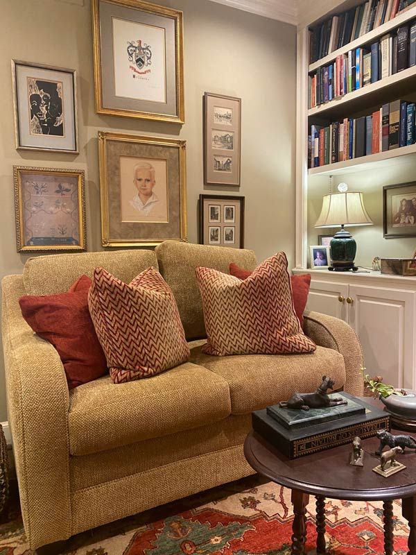 Cozy living room with a beige sofa, rust pillows, framed art, bookshelf, and round coffee table.