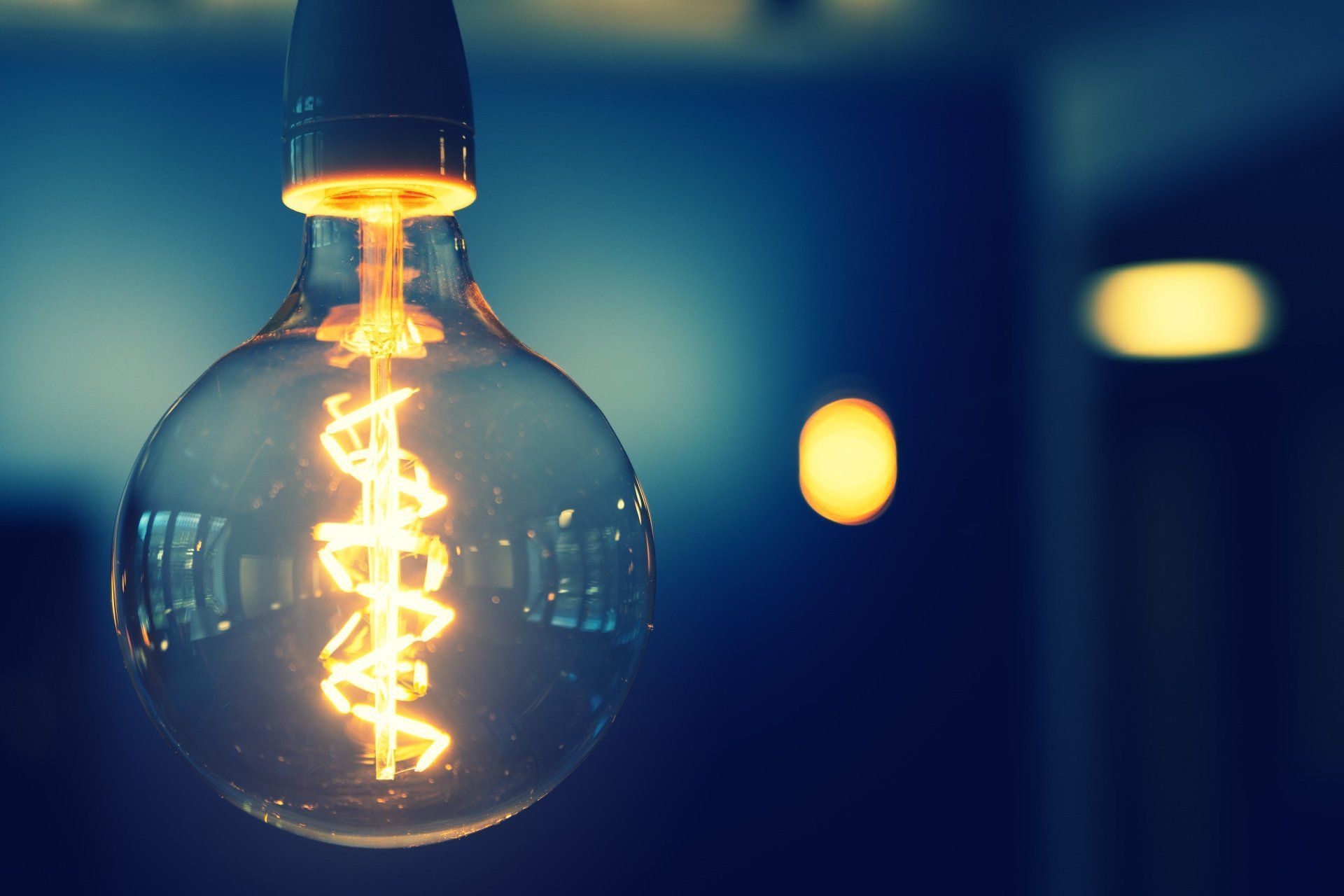 Close-up of a lit Edison-style lightbulb, glowing against a blurred, dark blue background.