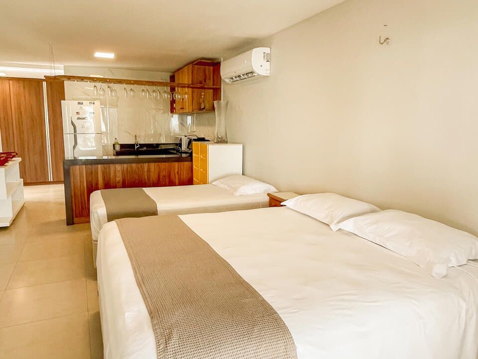 Quarto de hotel compacto com duas camas, kitchenette e paredes bege.